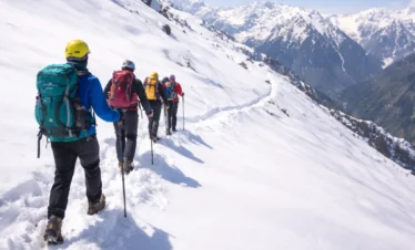 Snow trekking adventure in the Himalayas with a group of travelers hiking on a snowy mountain trail under clear blue sky